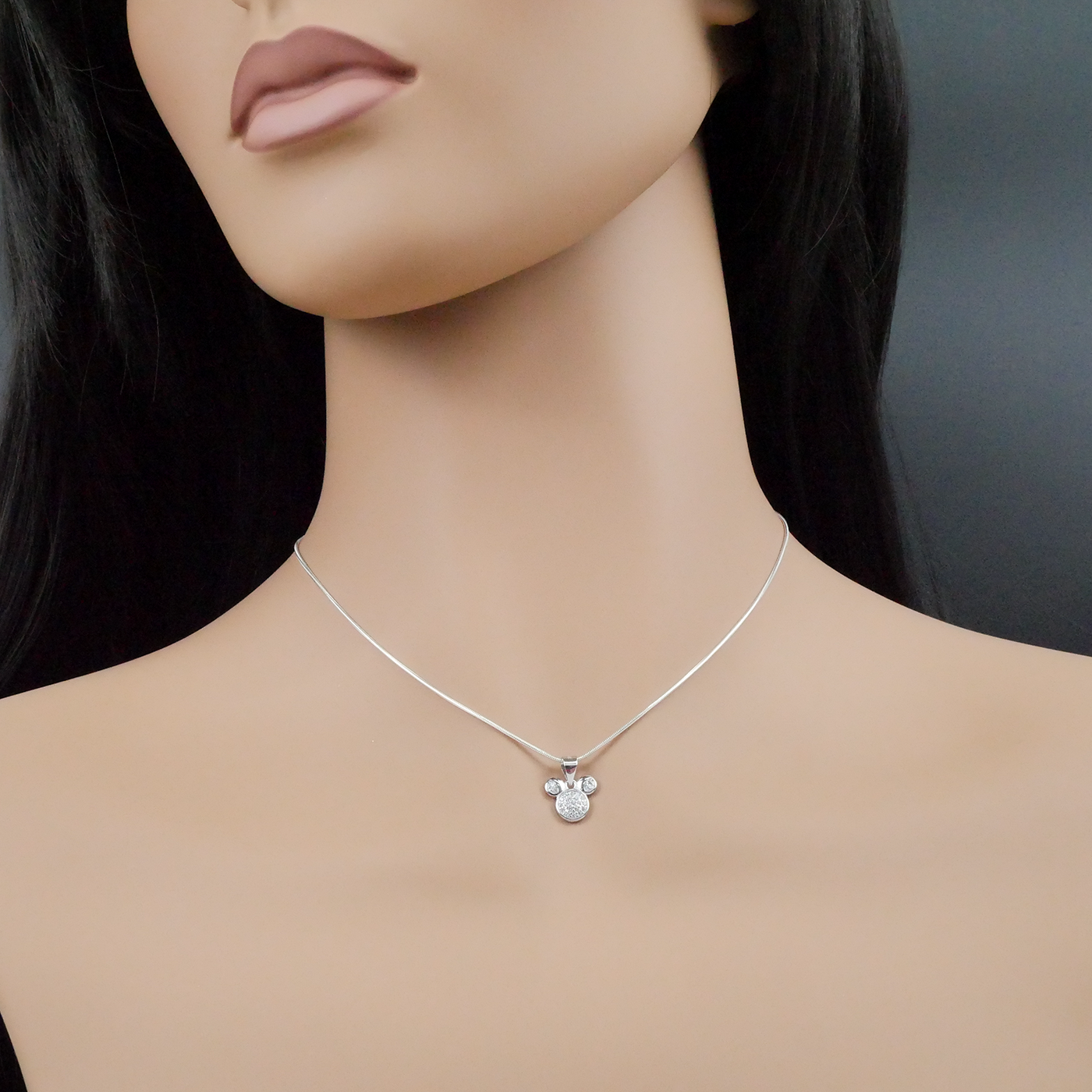 Mannequin wearing a silver necklace with a mouse-shaped pendant on a dark background