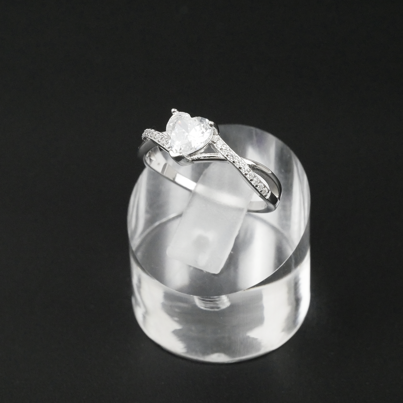 Silver ring with a heart-shaped gemstone on a clear stand against a black background
