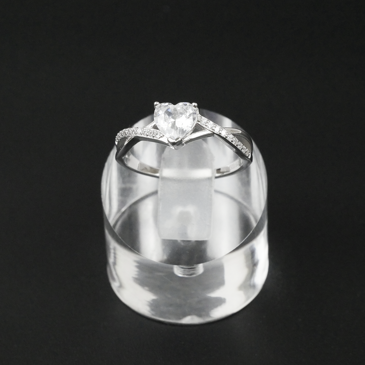 Silver ring with a heart-shaped gemstone on a clear stand against a black background
