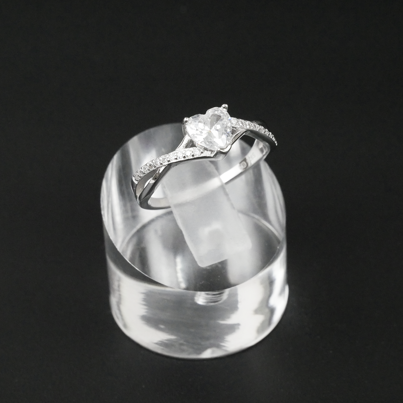 Silver ring with a heart-shaped gemstone on a clear stand against a black background