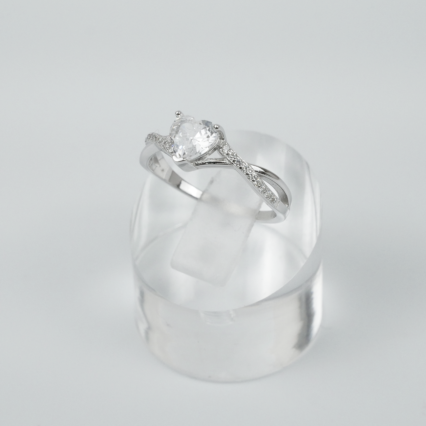 Silver ring with a heart-shaped gemstone on a clear stand against a light grey background