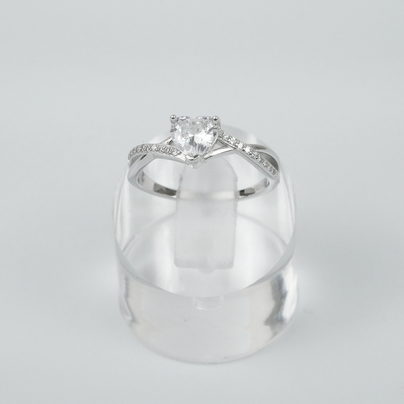 Silver ring with a heart-shaped gemstone on a clear stand against a light grey background