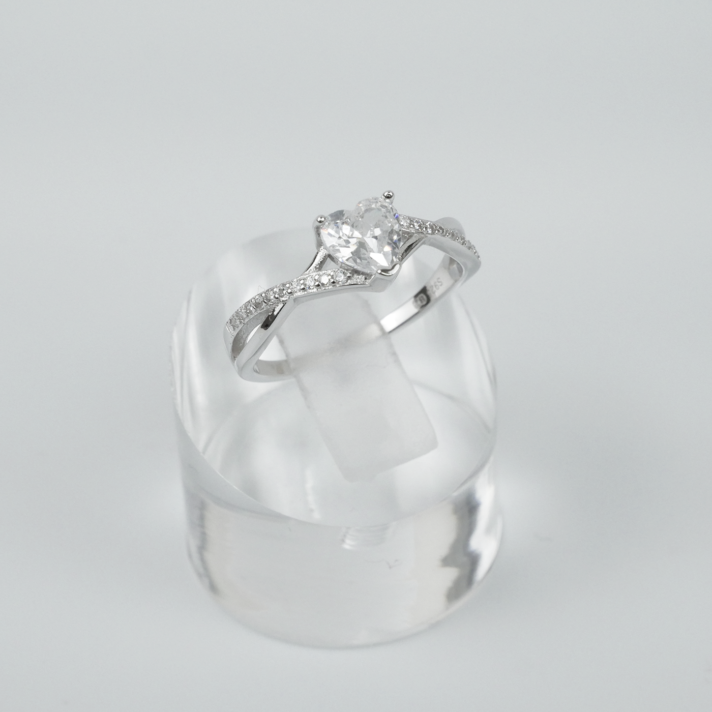 Silver ring with a heart-shaped gemstone on a clear stand against a light grey background