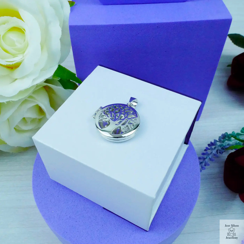 Silver pendant in a white box with purple lid, surrounded by flowers on a light wooden surface.