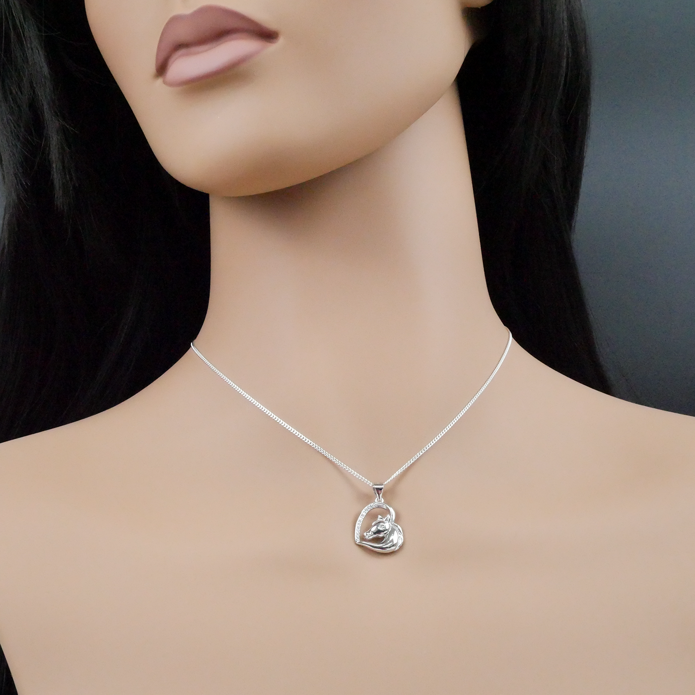 Mannequin wearing a silver necklace with a heart-shaped pendant against a dark background