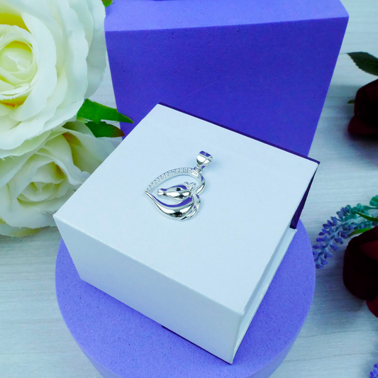 Silver pendant in a white box with purple interior, surrounded by flowers.