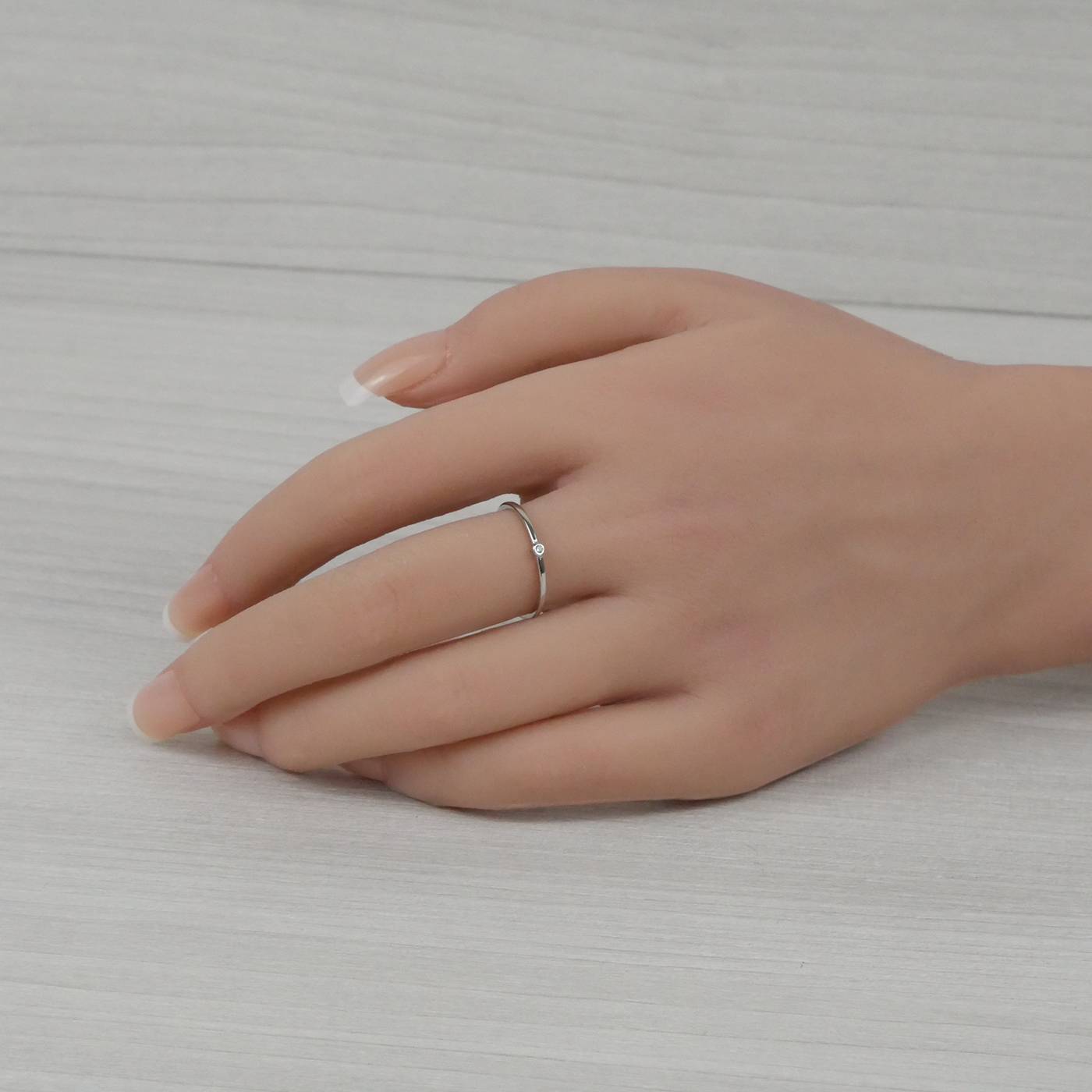 Hand wearing a silver ring on a neutral background