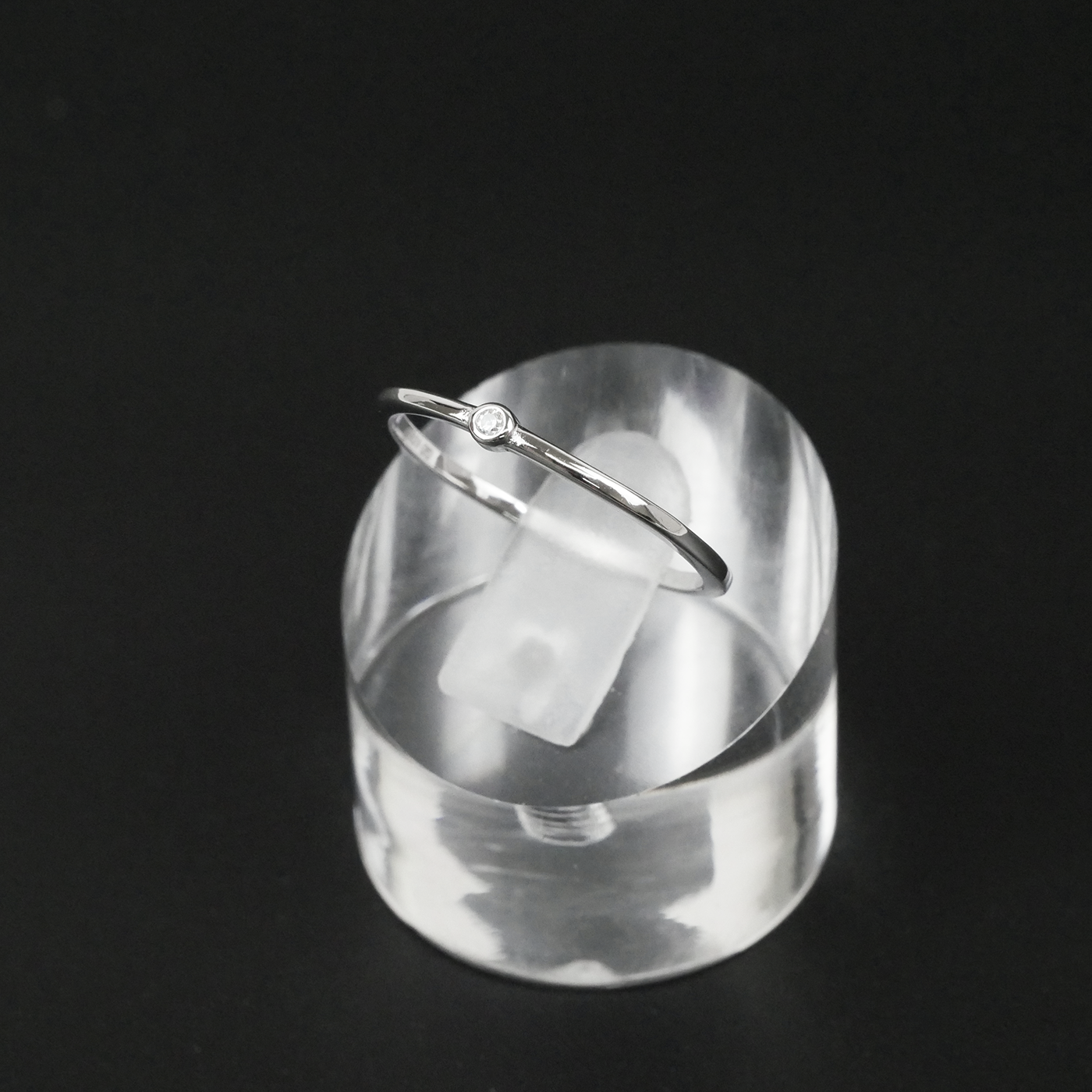 Silver ring on a clear acrylic stand against a black background