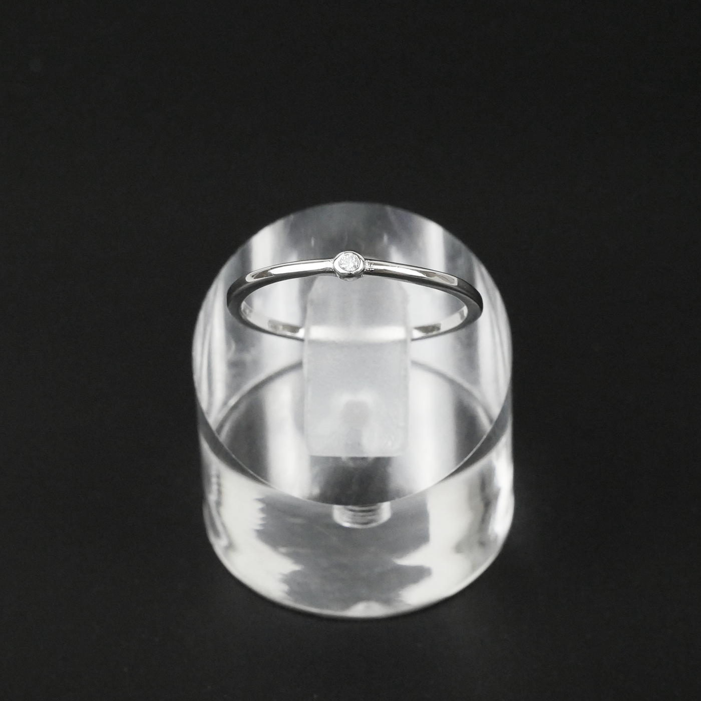 Silver ring on a clear acrylic stand against a black background