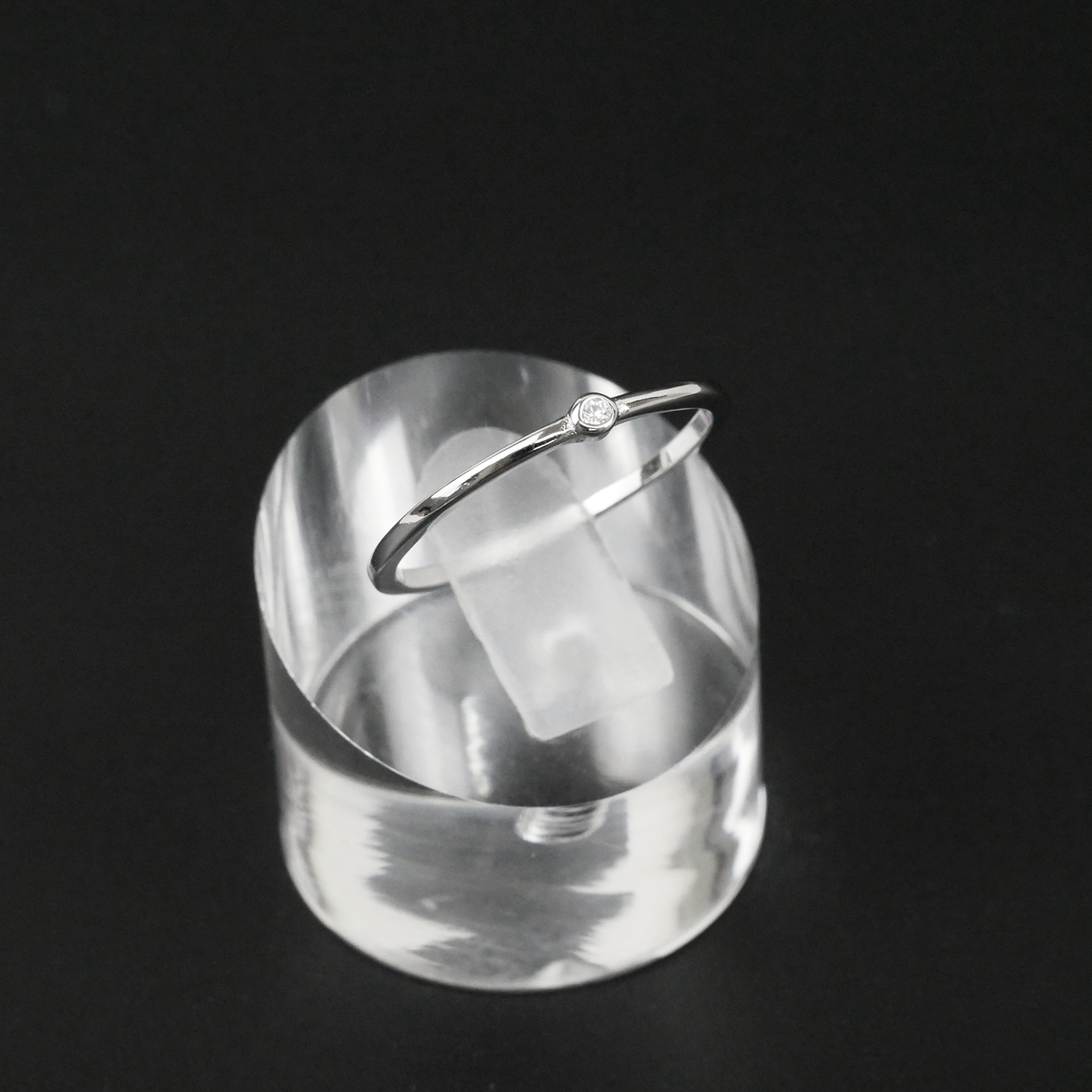 Silver ring on a clear acrylic stand against a black background