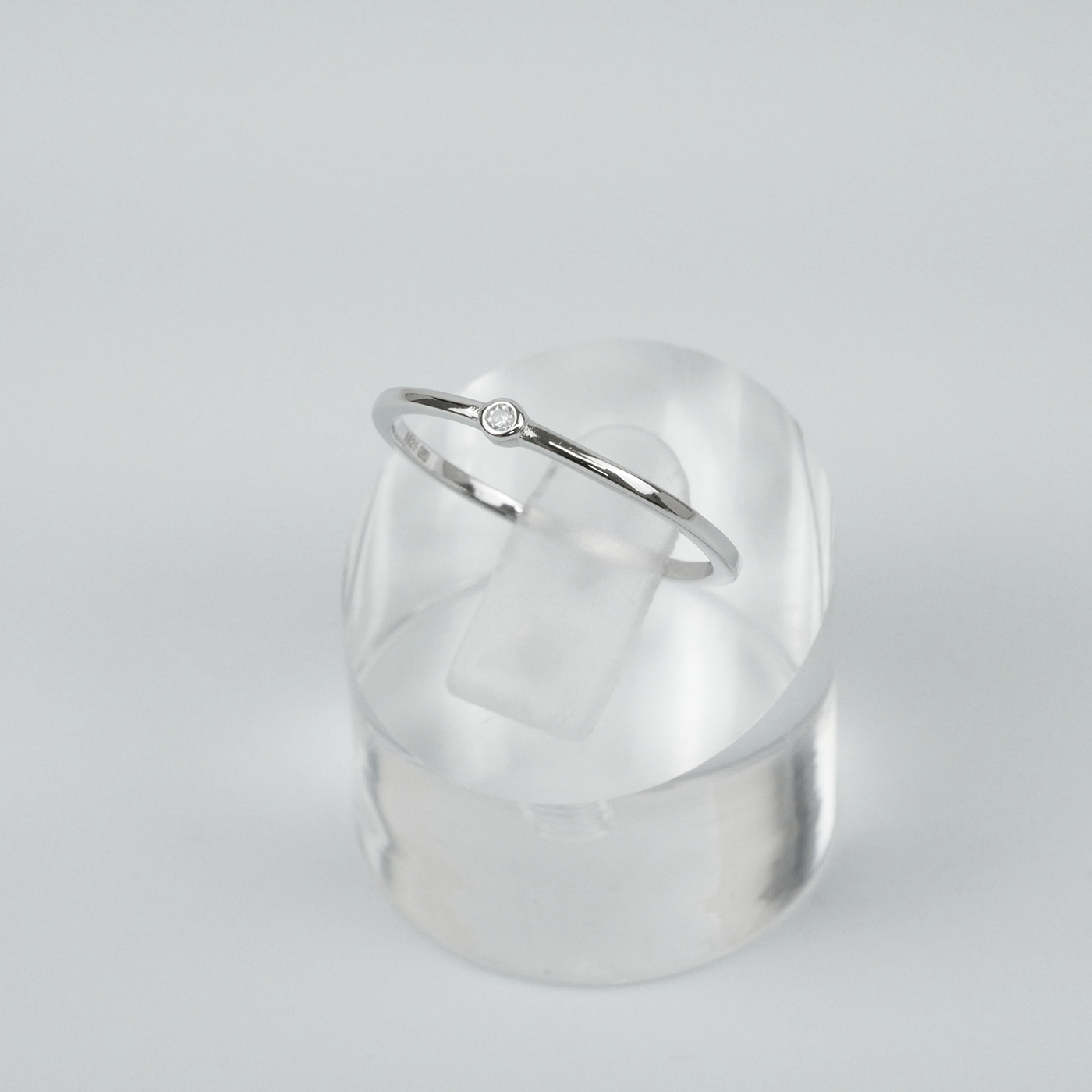 Silver ring on a clear acrylic stand against a light grey background
