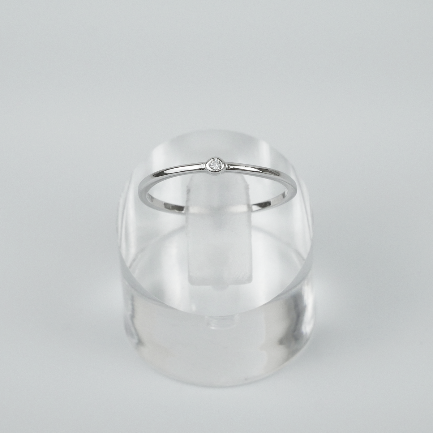 Silver ring on a clear acrylic stand against a light grey background