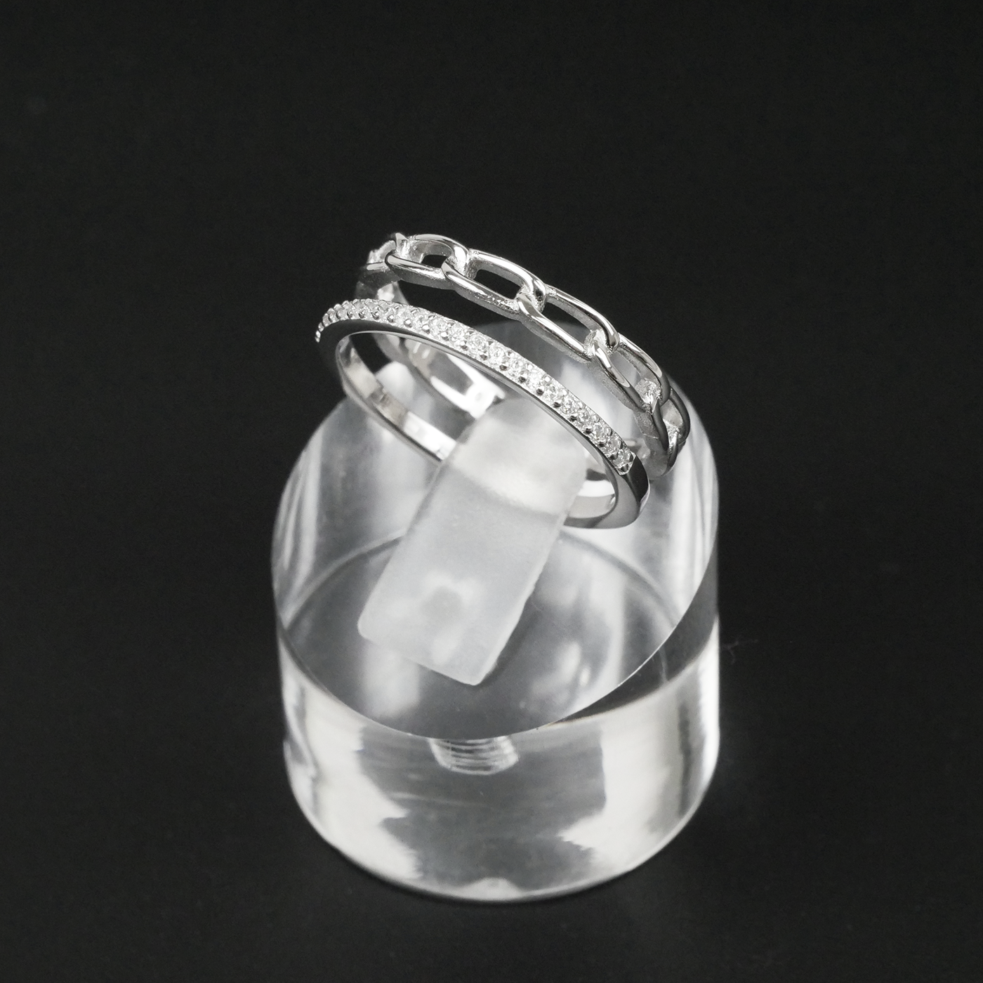 Silver ring with gemstones on a clear stand against a black background