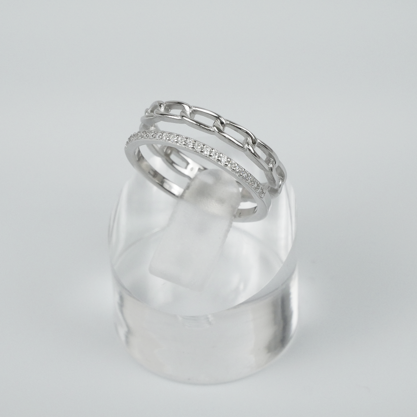Silver ring with gemstones on a clear stand against a light grey background