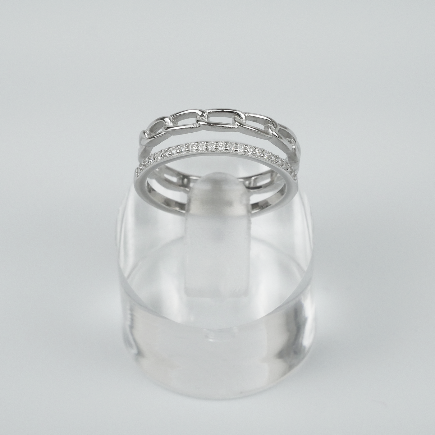 Silver ring with gemstones on a clear stand against a light grey background