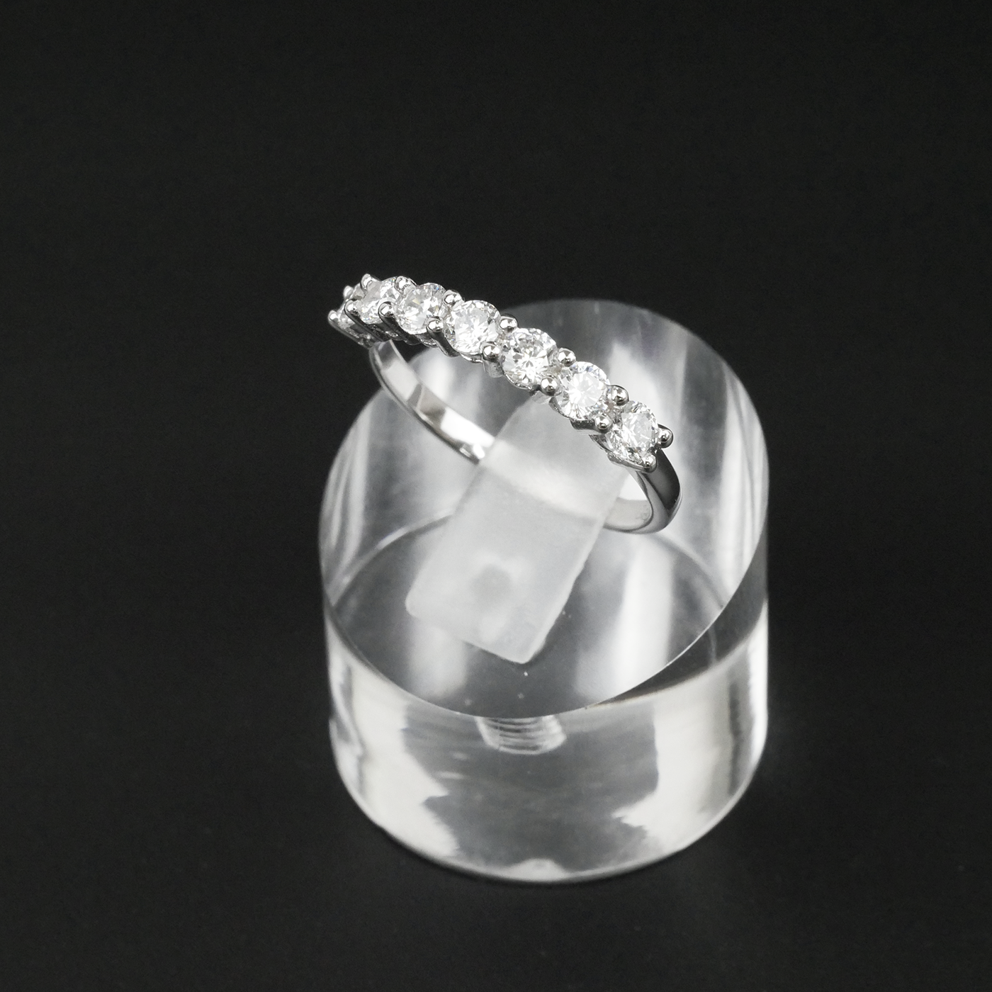 Silver ring with gemstones on a clear stand against a black background