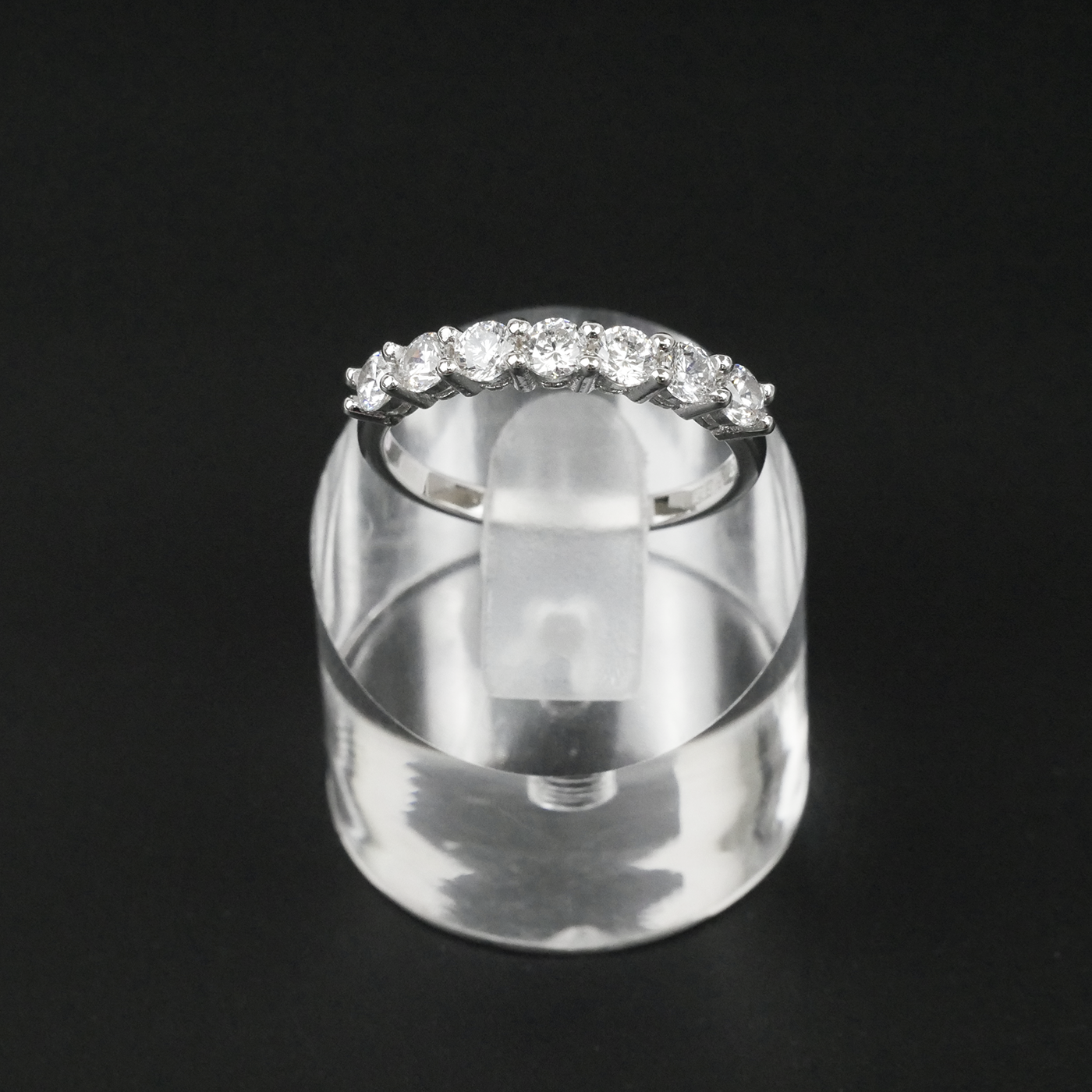 Silver ring with gemstones on a clear stand against a black background