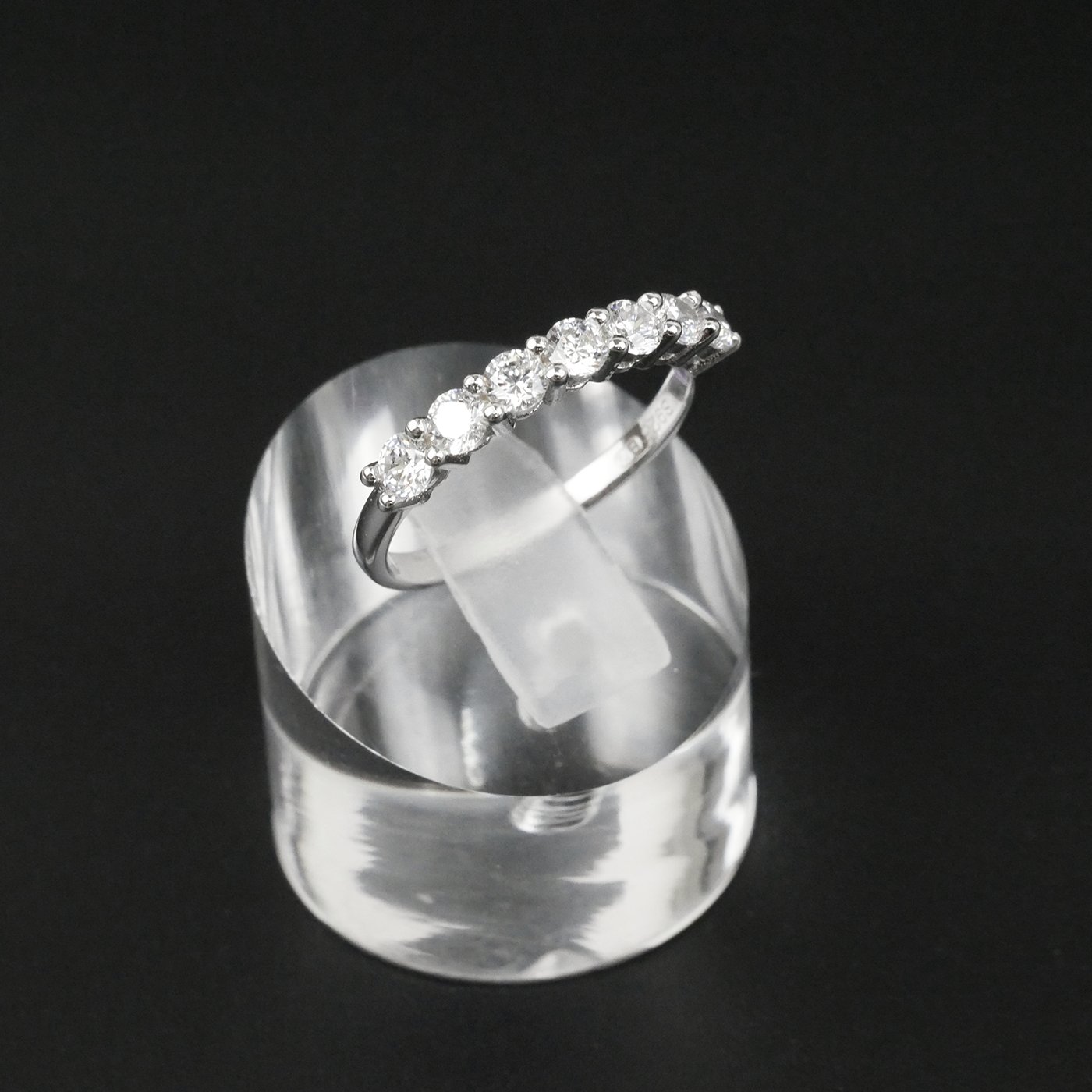 Silver ring with gemstones on a clear stand against a black background