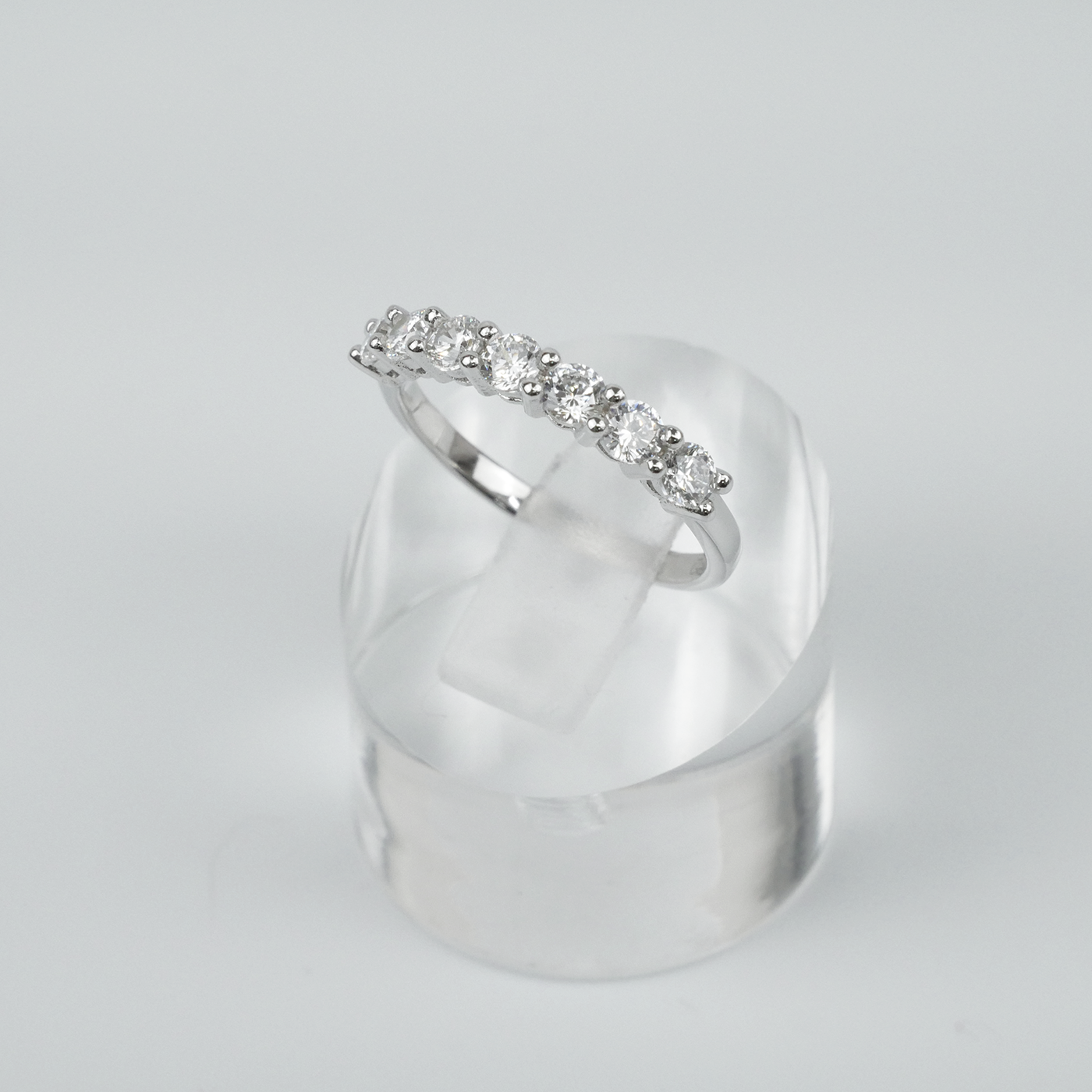 Silver ring with gemstones on a clear stand against a light grey background