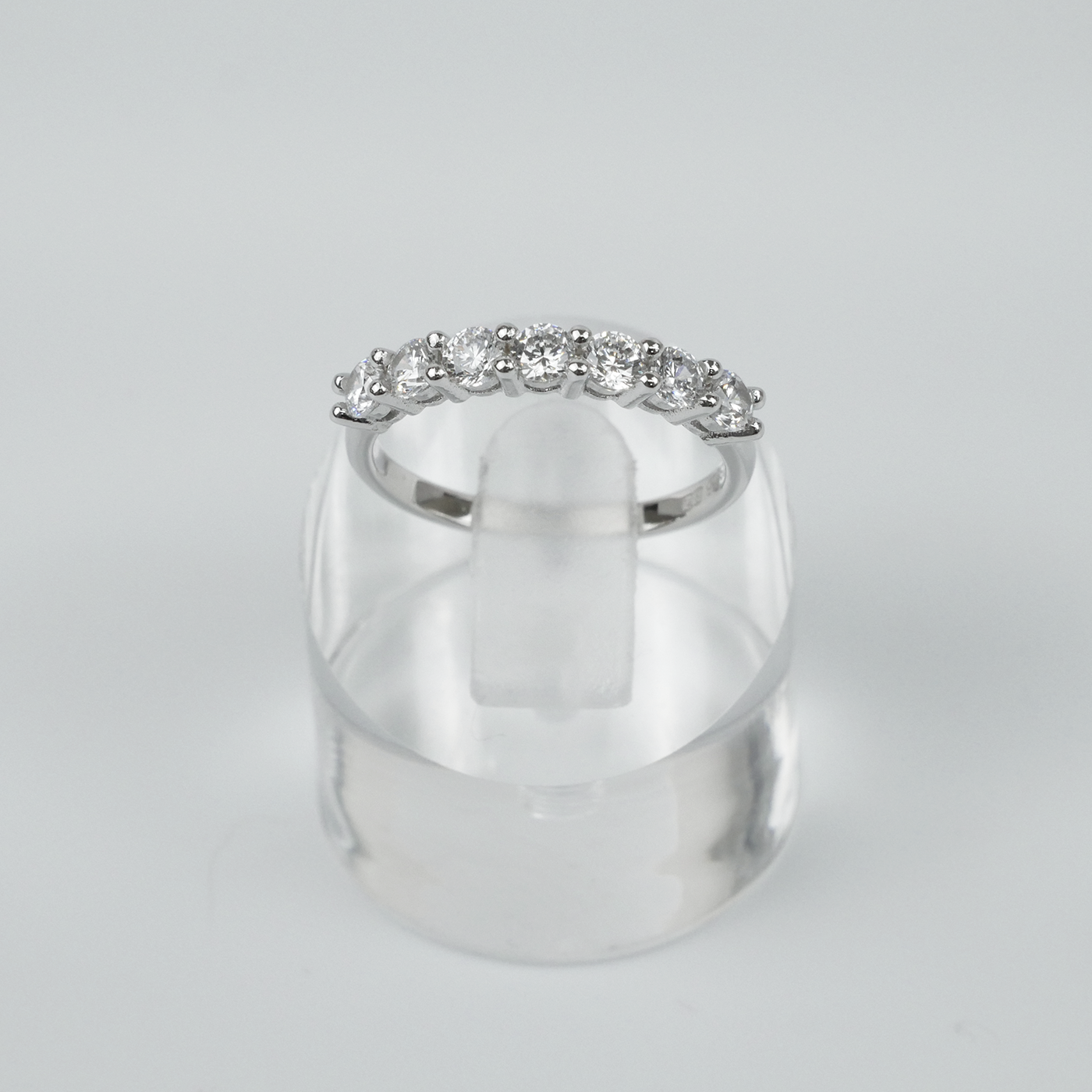Silver ring with gemstones on a clear stand against a light grey background
