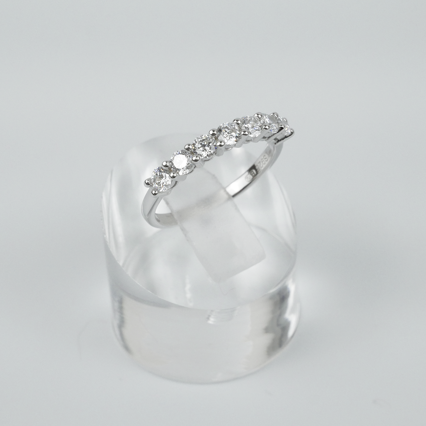 Silver ring with gemstones on a clear stand against a light grey background