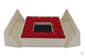 A luxury gift box with a flip-top lid, containing a ring of red roses around a jewelry box with a bow on top.