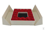 A luxury gift box with a flip-top lid, containing a ring of red roses around a jewelry box with a bow on top.