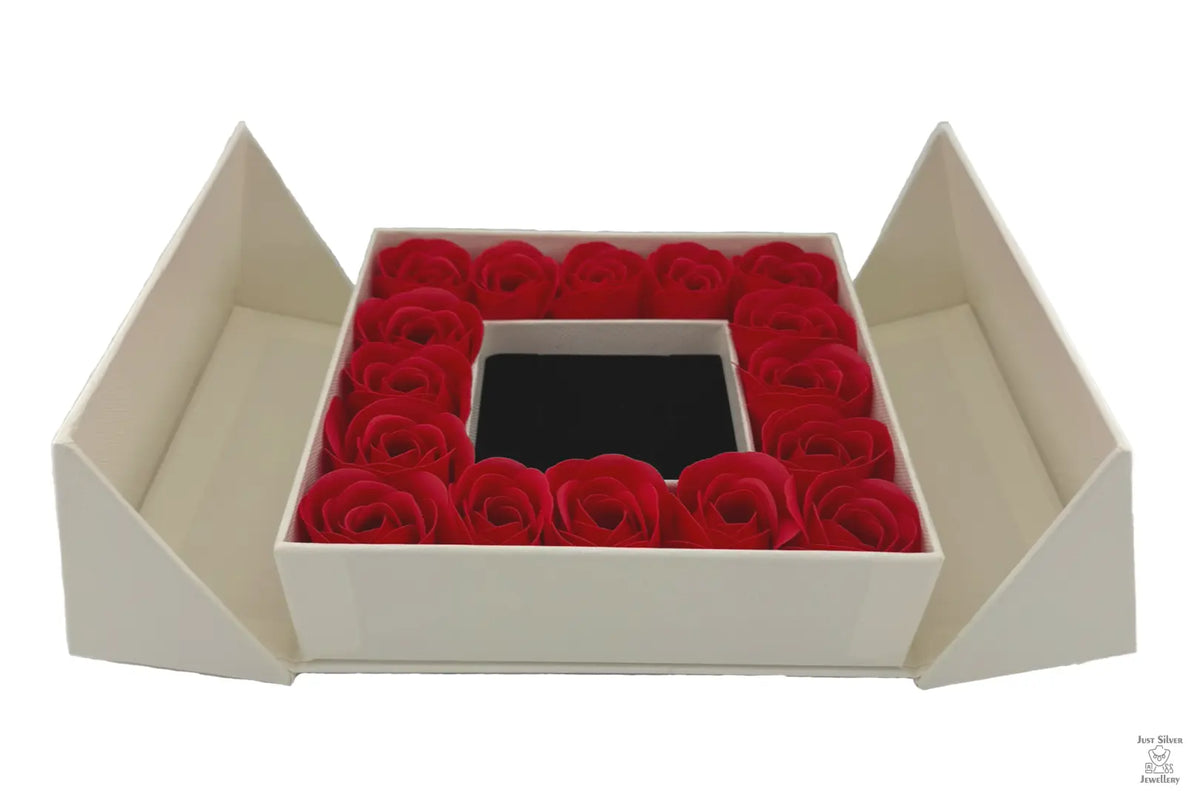 A luxury gift box with a flip-top lid, containing a ring of red roses around a jewelry box with a bow on top.